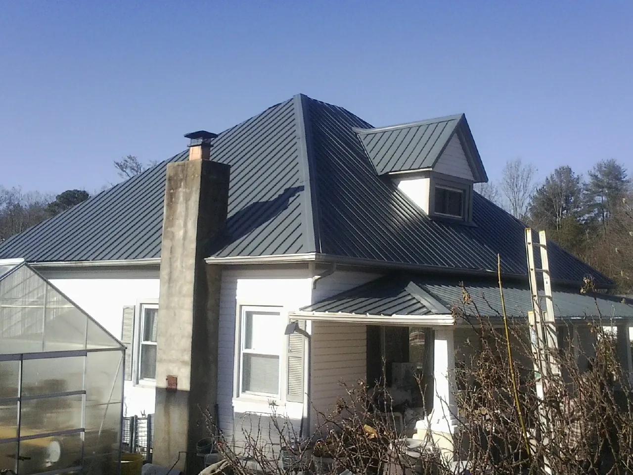 Dark blue standing seam metal roof on a white farmhouse with dormer — Slate & Tile Roof Repair by Roofing Brothers in Ridge