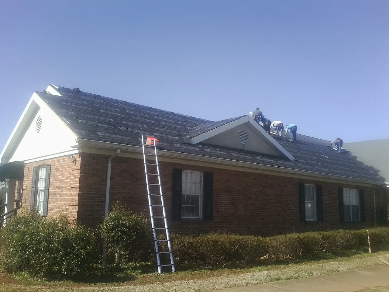 Crew tearing shingles off a brick ranch roof with a ladder set — Emergency Roof Repair work by our crew in Ridge