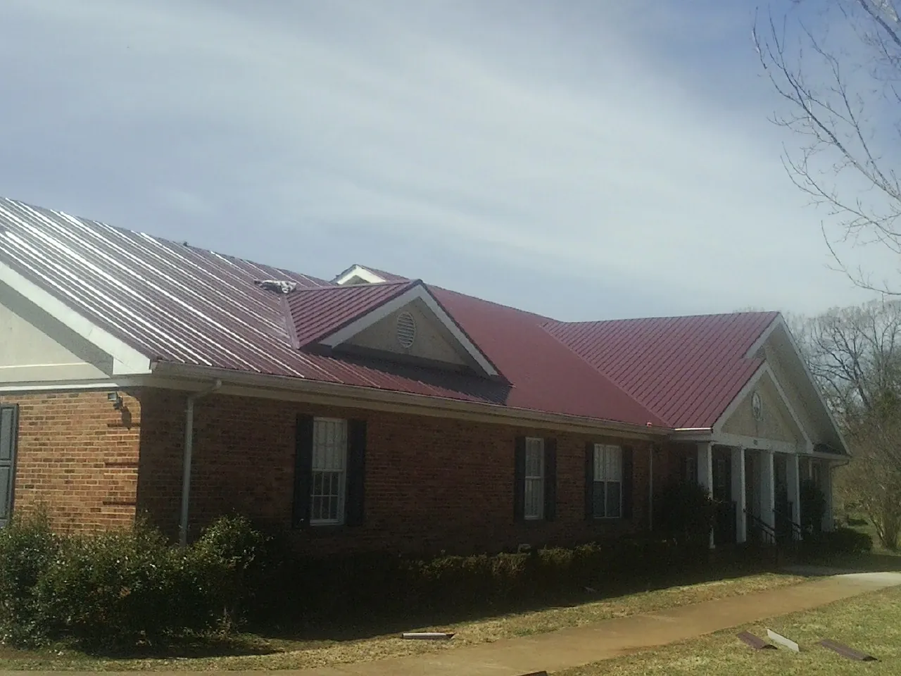 Red metal roof with gabled entries on a long brick building, from a Hail Damage Roof Repair job in Ridge