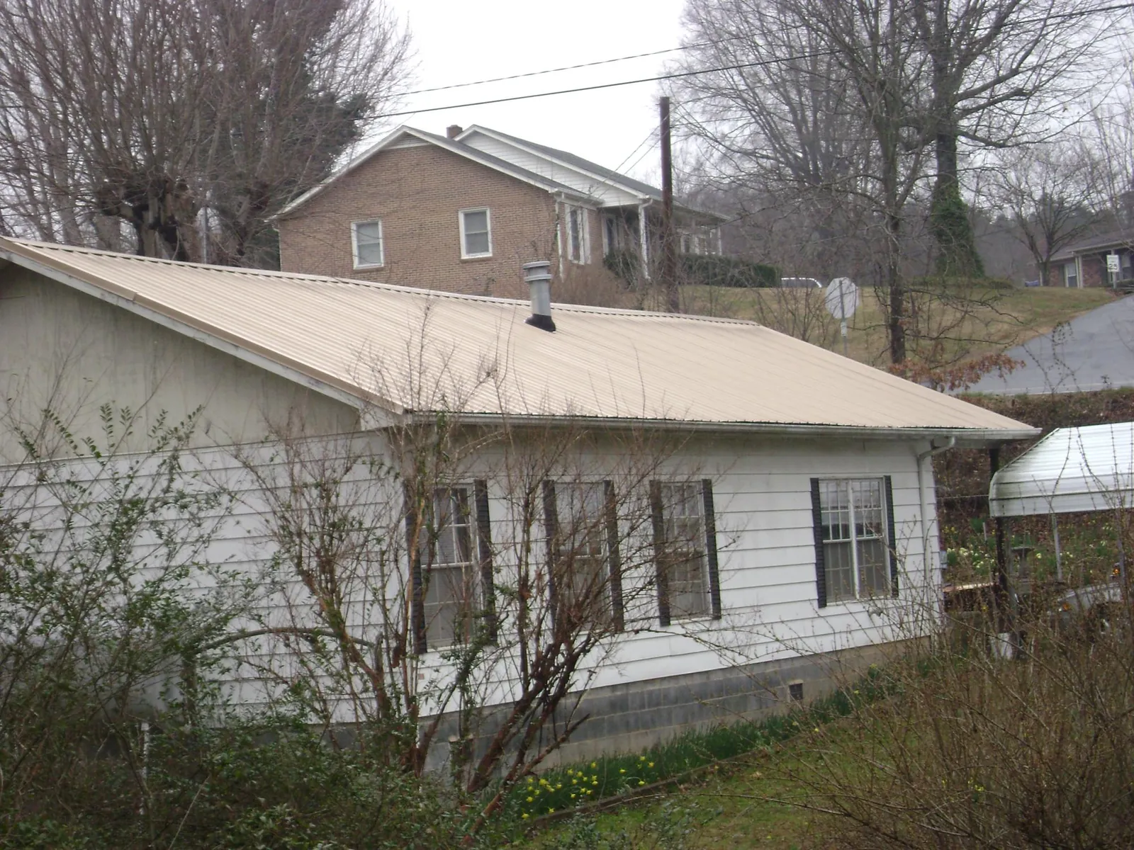 Tan metal roof on a white sided house set into a hillside — Commercial Roofing by Roofing Brothers in Ridge