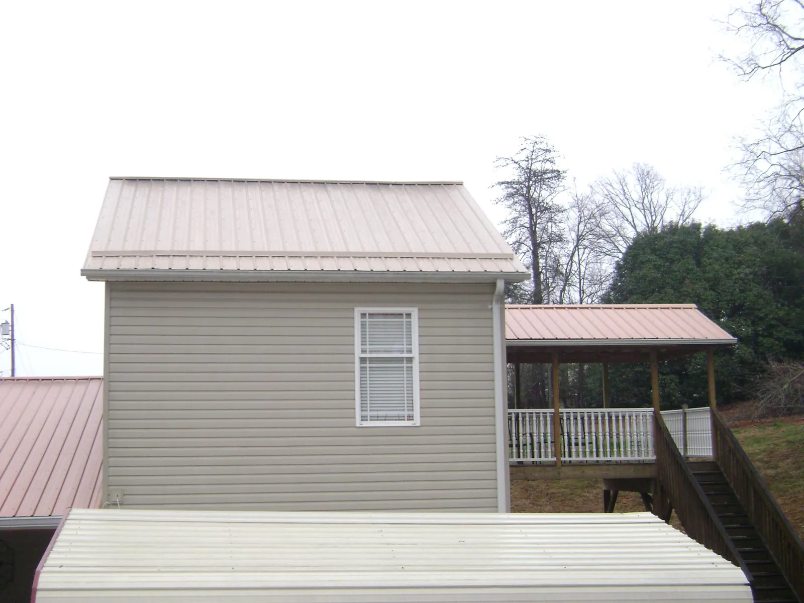 Tan metal roofs on a two story addition and attached porch, from a Roof Replacement job in Ridge